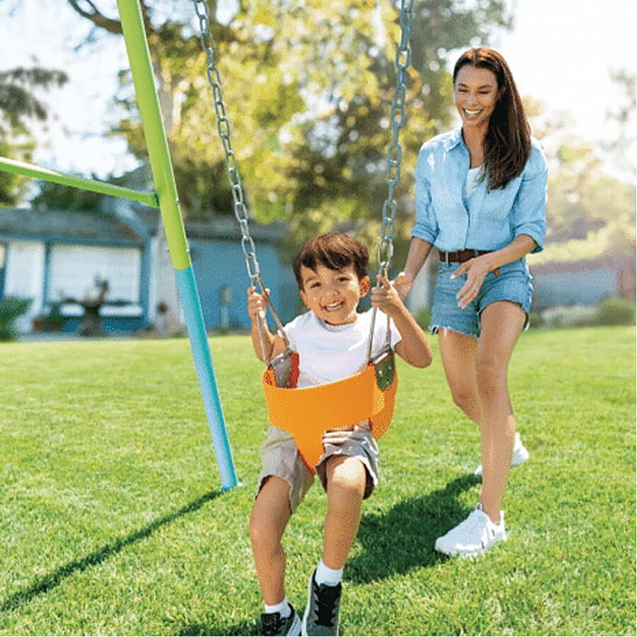 ילד מתנדנד בנדנדה בחצר כשאישה דוחפת מאחור על דשא ירוק | yrz