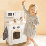 ילדה משחקת ליד מטבח עץ לילדים בצבע לבן עם כיריים, תנור ואביזרים | yrz
