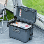 צידנית קשיחה של Coleman עם מכסה פתוח, מלאה בקרח ומשקאות ליד אוהל קמפינג | yrz