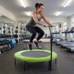 אישה קופצת על טרמפולינת ספורט ירוקה בחדר כושר | yrz טרמפולינות