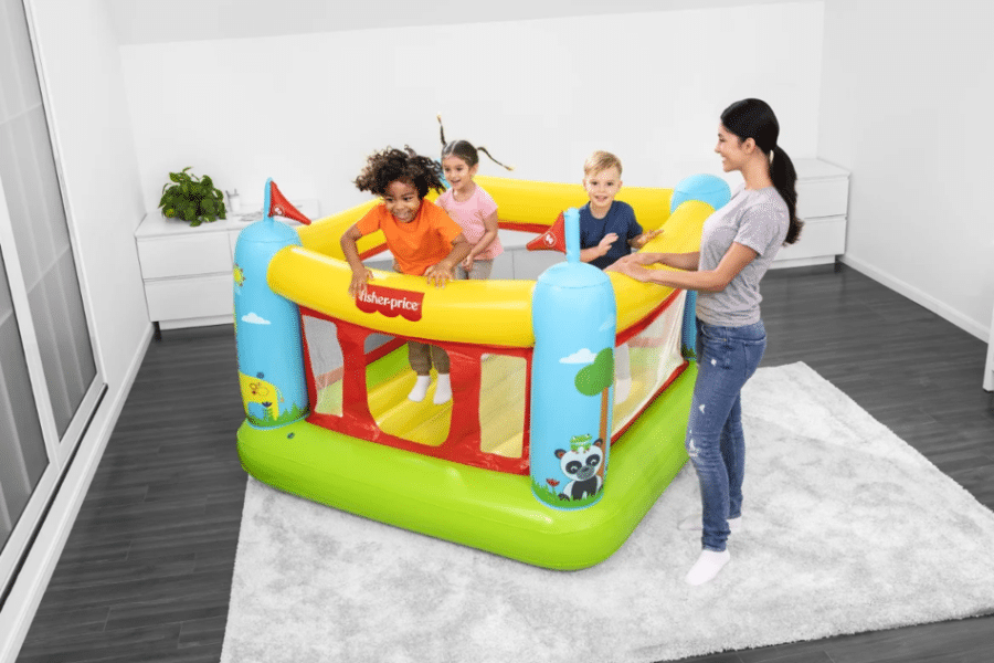 שלושה ילדים משחקים במתנפח קטן צבעוני עם דפנות רשת, לידם אישה בחדר | yrz